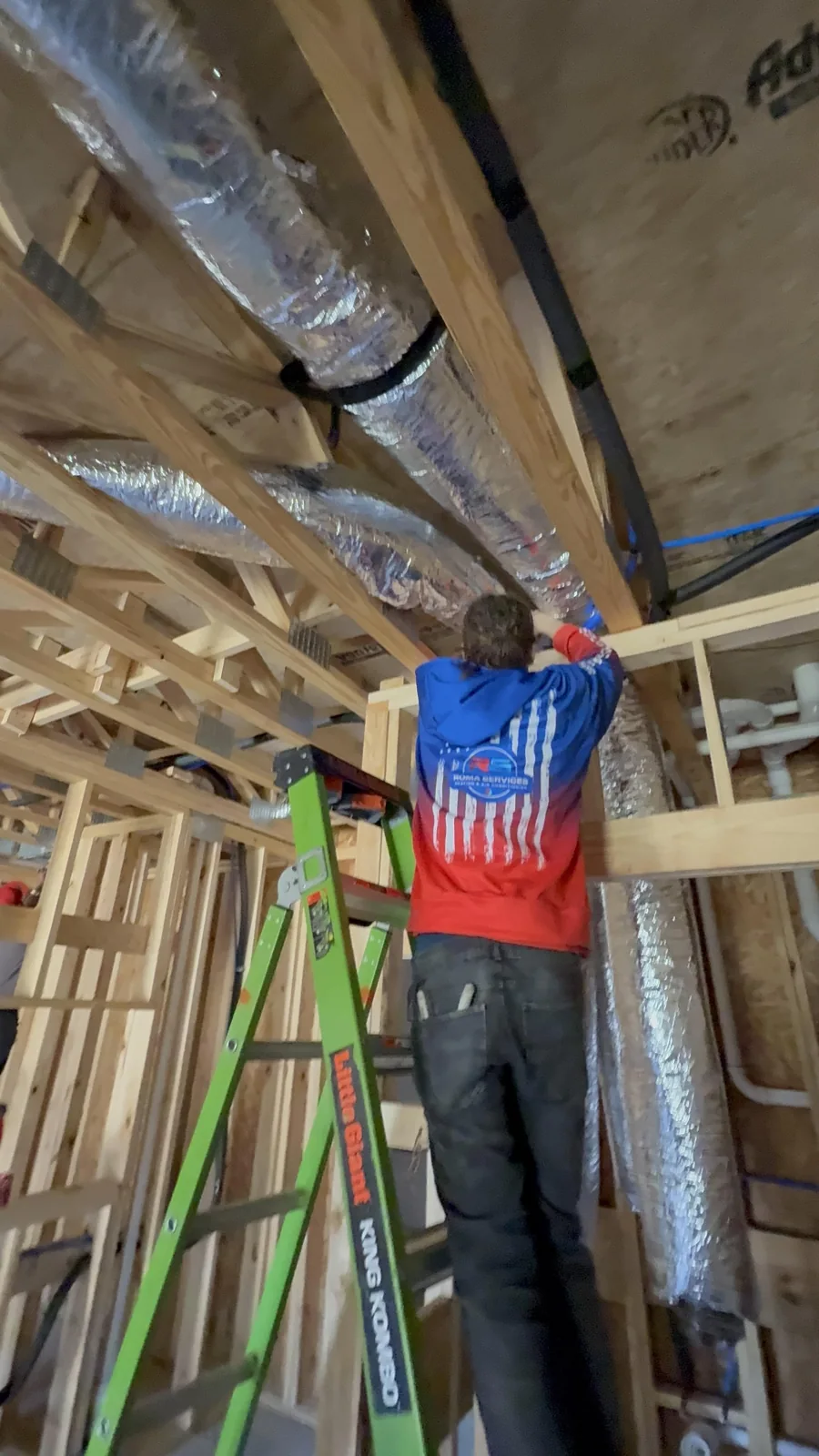 Roma technician installing overhead ductwork in a framed interior